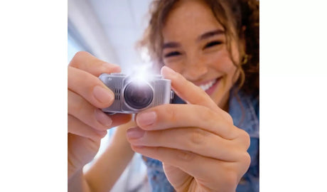 Person holding a silver Photo Creator Mini Cam with the flash illuminated