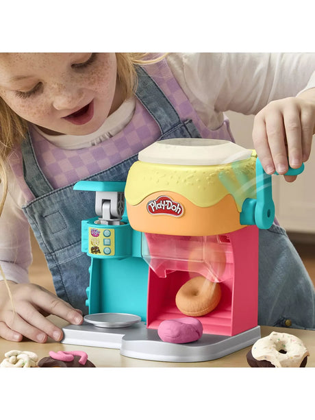Child using the Play-Doh Donut Drop Shop Playset with doughnut machine and Play-Doh doughnuts on a table