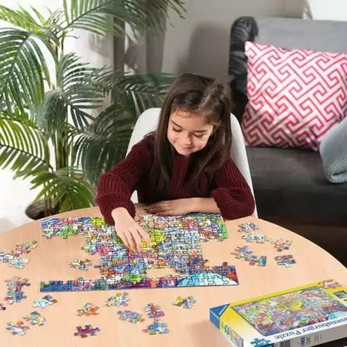 Child assembling the Ravensburger A Day in Chaosville jigsaw puzzle on a table with loose pieces surrounding the colourful town scene