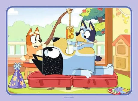 Bluey, Bingo, and Bandit playing together outdoors on a wooden deck with a piece of cheese on a stick