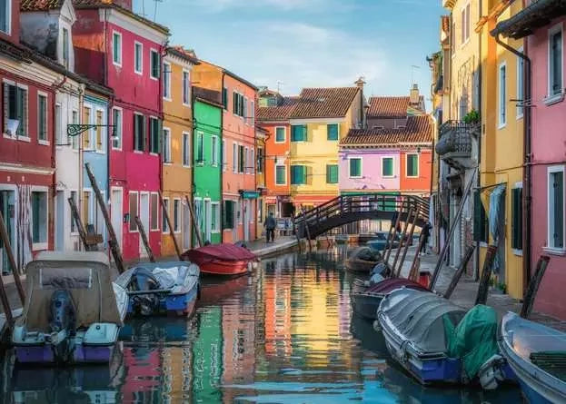 Ravensburger Burano Italy puzzle artwork showing brightly coloured canal houses, boats, a footbridge and reflections in the water