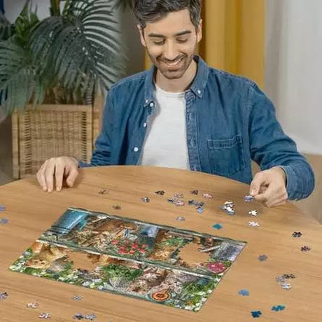 Man assembling the Ravensburger Cats on the Shelf jigsaw puzzle on a table with loose pieces around the cat artwork
