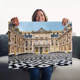 Woman holding the completed Ravensburger Château de Versailles puzzle showing the palace courtyard and black and white paving