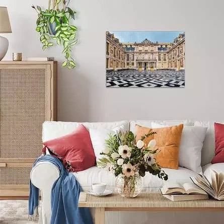 Completed Ravensburger Château de Versailles puzzle displayed on a living room wall above a white sofa