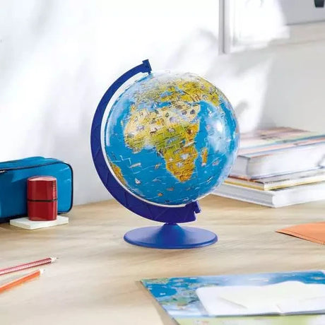 Ravensburger Children’s World Map 3D Puzzle globe displayed on a desk beside books, pencils and stationery