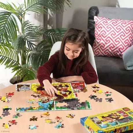 Child assembling the Ravensburger Donkey Kong 100 piece XXL jigsaw puzzle on a table with loose puzzle pieces nearby