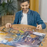 Man assembling the Ravensburger New York Summer and Winter jigsaw puzzle on a table with loose pieces around the image