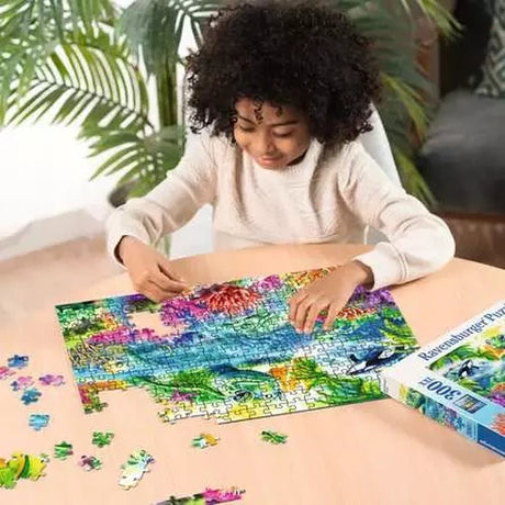 Child assembling the Ravensburger Ocean Treasures jigsaw puzzle on a table with colourful sea life pieces around the puzzle