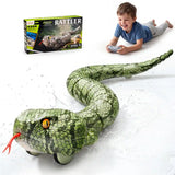 Green remote control snake with detailed scales, yellow eyes and red forked tongue, shown with water splashes. A boy holding a grey controller and the Rattler retail box appear above the snake.