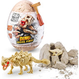 Robo Alive Dino Fossil Find egg packaging with dinosaur skull graphic, gold hammer, dinosaur skeleton figure and broken rock pieces on white background