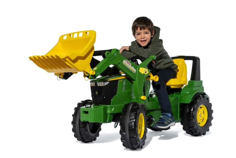 Child riding the Rolly Farmtrac John Deere 7310R toy tractor with front loader raised on a white background