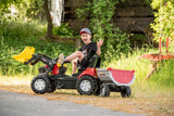 Child towing the grey Rolly Halfpipe Single Trailer behind a pedal tractor while smiling outdoors.
