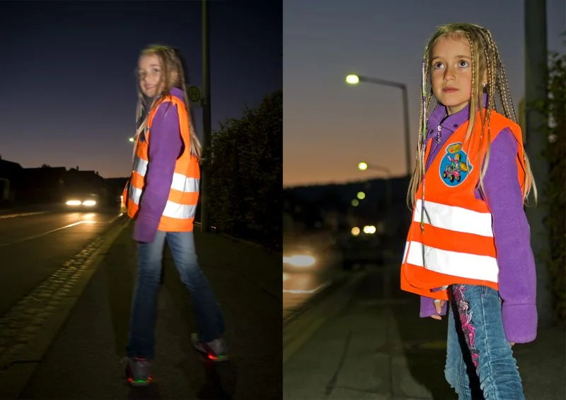 Child wearing the Rolly Hi Vis Safety Vest while walking on a street at dusk with headlights in the background