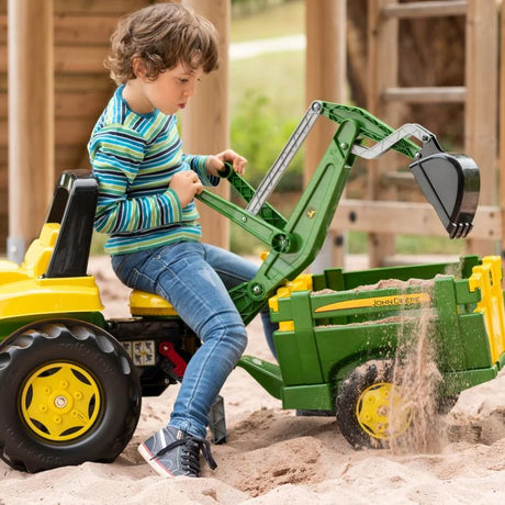 Child operating a Rolly John Deere backhoe digger attachment on a ride on tractor while scooping and dumping sand