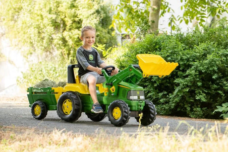 Child riding the Rolly Junior John Deere pedal tractor with front loader and trailer outdoors on a sunny path