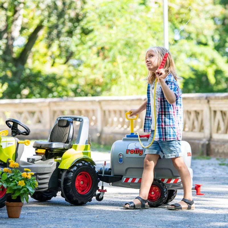 Child playing outdoors with a Rolly tanker trailer attached to a pedal tractor

