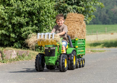 Child driving a Rolly tractor outdoors using the Timber Loader to carry a bundle of hay