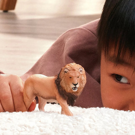Schleich African Lion figure being held on a soft white surface in front of a child