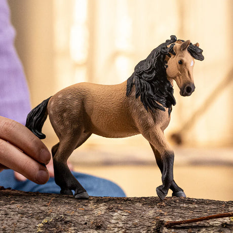 Schleich Andalusian Mare figure standing on a piece of bark with a hand visible behind it.