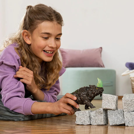 Child holding the Schleich Battle Rhino figure beside stacked grey blocks on a wooden table