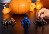 Schleich Blue Poison Dart Frog figure positioned between a tarantula and a scorpion with orange pumpkins behind.