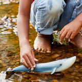 Schleich Blue Whale figure in shallow water beside a child’s hand and bare feet