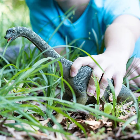 Close-up of a child holding the Schleich Brachiosaurus figure among tall grass