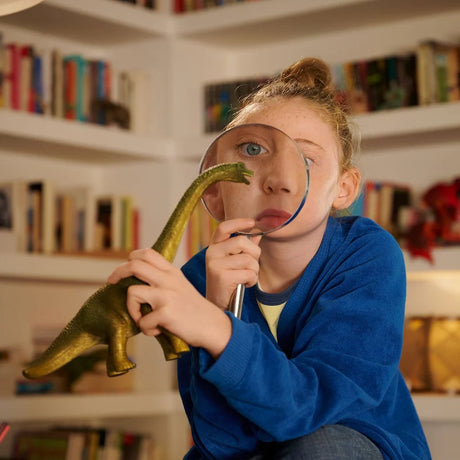Child examining the head of the Schleich Brachiosaurus figure through a magnifying glass