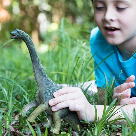 Child holding the Schleich Brachiosaurus figure upright in grass, showing its long neck and open mouth