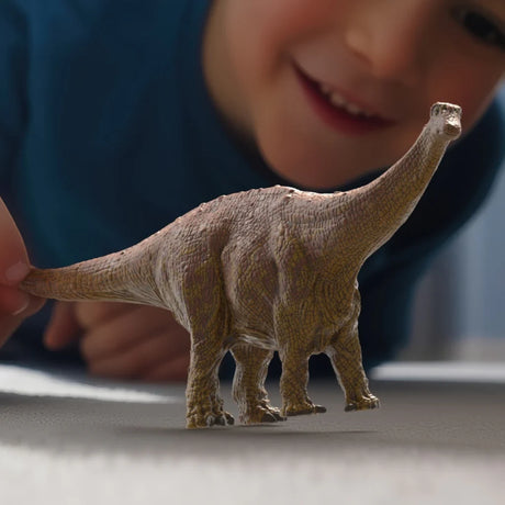 Schleich Brontosaurus figure being moved by a hand with child visible behind it