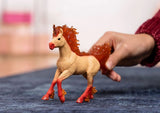 Schleich Elementa Fire Unicorn Stallion figure standing on a blue surface with a hand holding its tail