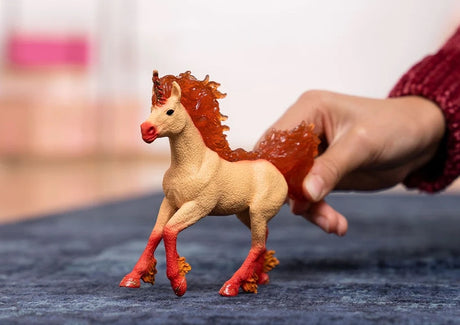 Schleich Elementa Fire Unicorn Stallion figure standing on a blue surface with a hand holding its tail