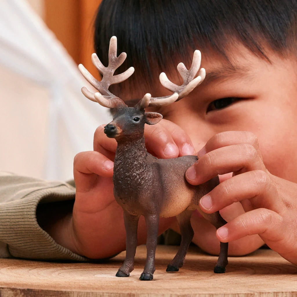 Child holding the Schleich Elk figure on a wooden surface