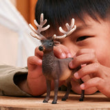 Child holding the Schleich Elk figure on a wooden surface