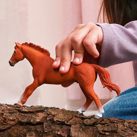 Schleich English Thoroughbred Stallion figure standing on bark beside a hand