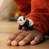 Schleich Giant Panda Cub figure standing on a hand with a red sleeve visible behind it.