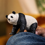 Schleich panda figure shown resting on a person’s knee, displaying its black and white markings and textured sculpt.