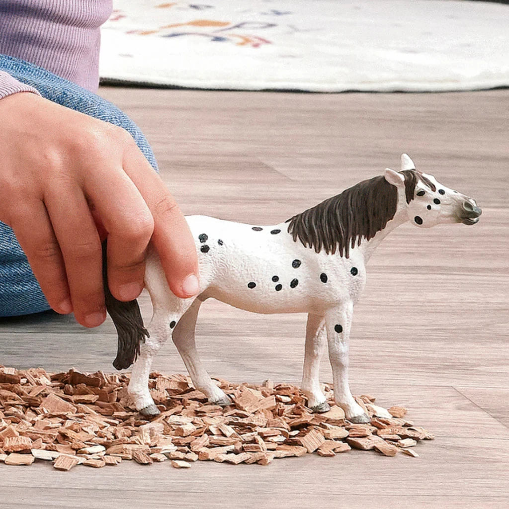 Schleich Knabstrupper Gelding figure being held in a play scene with wood chip bedding