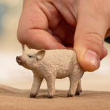 A Mangalica piglet figurine with a curly textured coat and a hand touching its back in a playful motion.