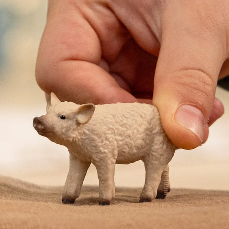 A Mangalica piglet figurine with a curly textured coat and a hand touching its back in a playful motion.