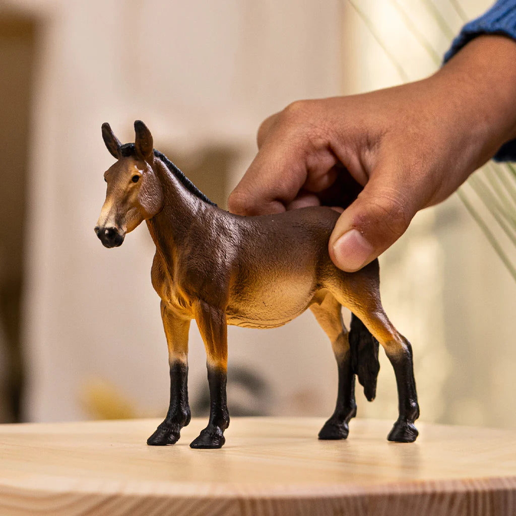 Schleich Mule figure standing on a wooden surface while a hand holds its back.
