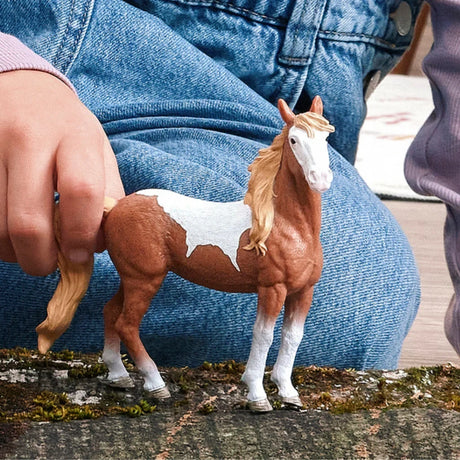 Schleich Mustang Mare figure standing on wood beside a hand
