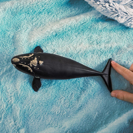 Schleich North Atlantic Right Whale figure on blue fabric beside a hand, showing the size of the whale figure