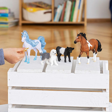 Schleich Old English Sheepdog figure standing on a white wooden crate between a blue horse and a black calf, with a brown horse beside them