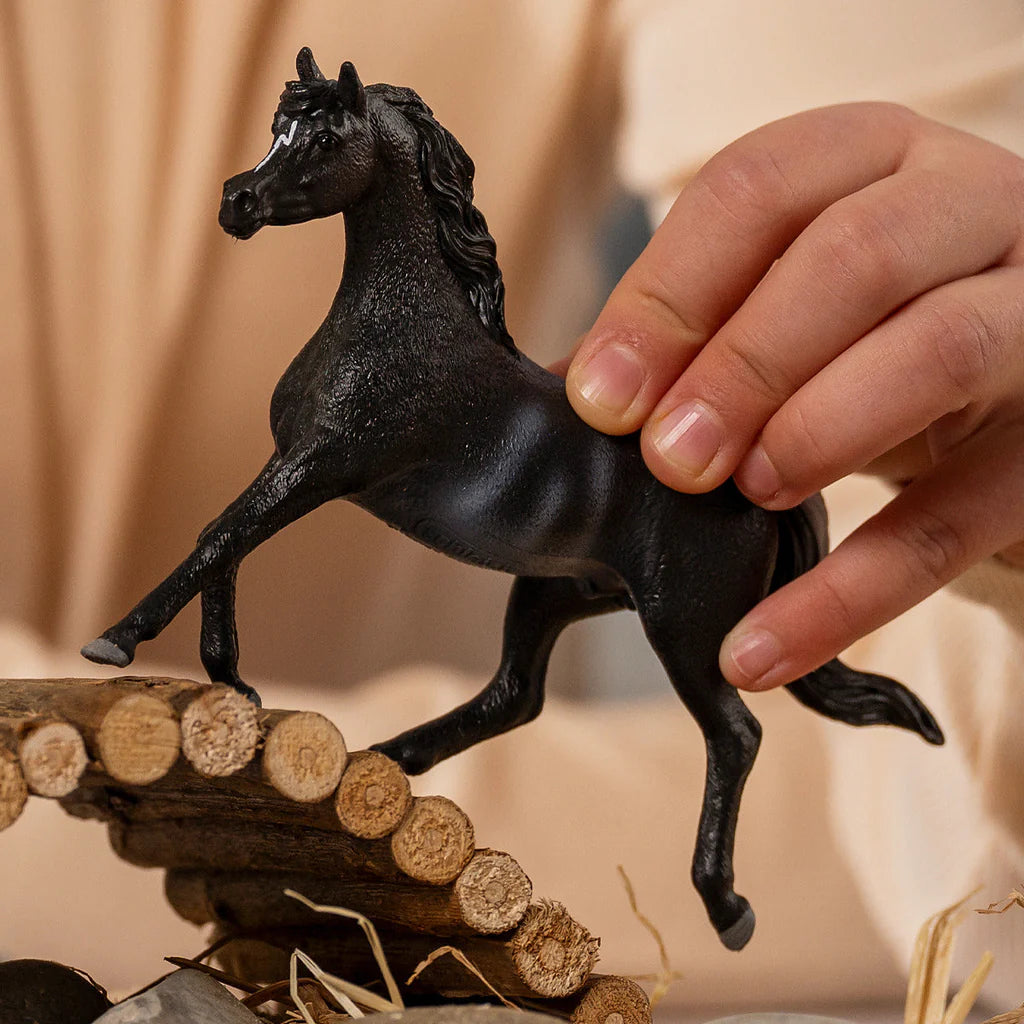Schleich Rabicano Arabian Stallion figure held above a small log bridge with one front leg extended.