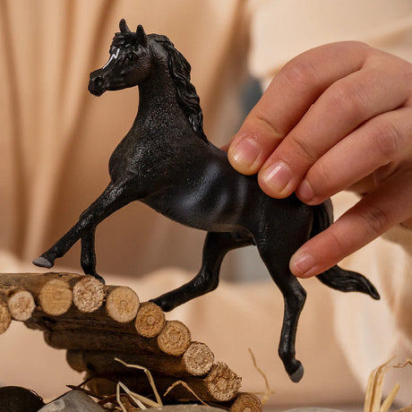 Schleich Rabicano Arabian Stallion figure held above a small log bridge with one front leg extended.