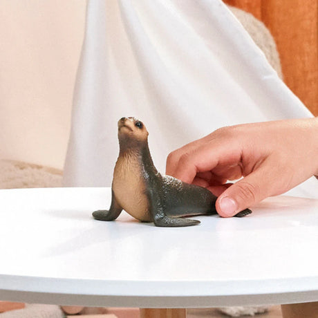 Schleich Sea Lion figure beside a hand on a white table, showing its raised head and front flippers