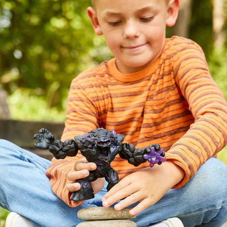 Child holding the Schleich Shadow Stone Monster figure above two stacked stones outdoors