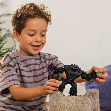Child holding the Schleich Shadow Stone Monster figure above a stone block while placing small stones in its hands