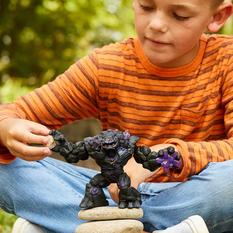 Child holding a small stone beside the open hand of the Schleich Shadow Stone Monster figure standing on stacked stones